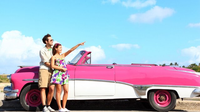 Couple leaning on pink convertible. 