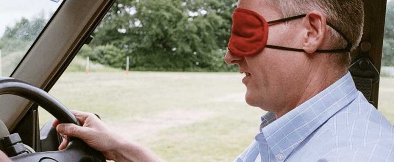 A man driving with a blind fold over his eyes.