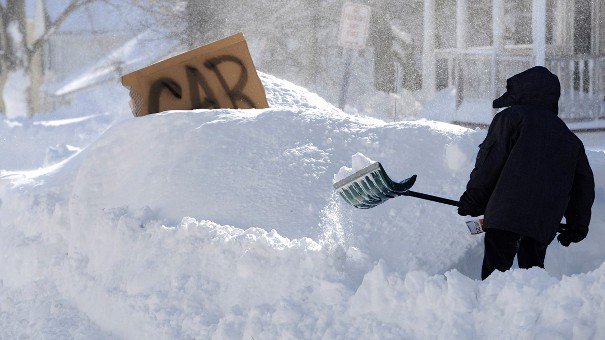 Car buried in show person trying to dig it out.